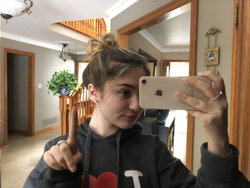 A person with short hair in a bun takes a selfie in a hallway.