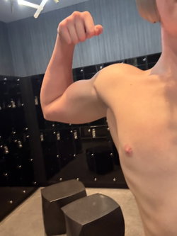 A muscular person flexes their bicep in a gym setting.