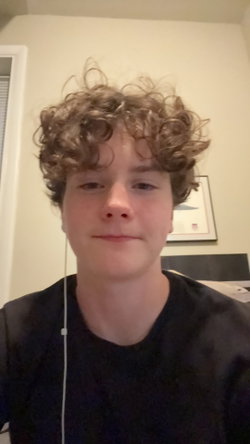 Person with curly hair in a black shirt standing indoors.