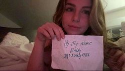 A blonde woman with a nose ring holds a note while lying on a bed.