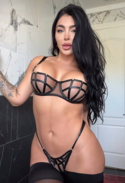 Woman with long dark hair in a black lace bra and matching thong.