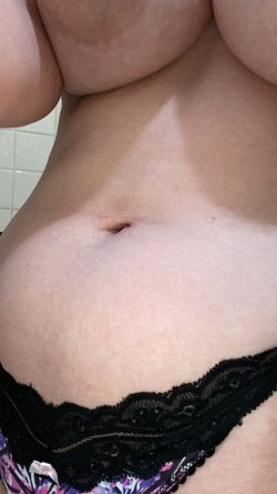 Close-up of a person's midsection showing bare stomach and lower chest, wearing black lace-trimmed underwear with