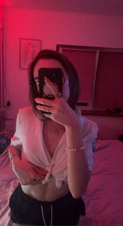A woman with shoulder-length dark hair takes a mirror selfie in a dimly lit room with red lighting, wearing a white