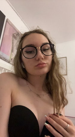 A woman with glasses and long hair poses in a black bra.