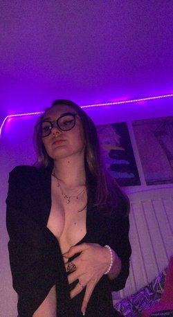 Brunette woman with glasses in a black blazer, posing in a room with purple LED lighting.