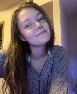 A brunette woman with a nose ring smiles softly in a cozy, dimly lit room.