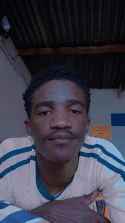 Close-up selfie of Black man with mustache wearing blue-striped shirt in room with metal roof.