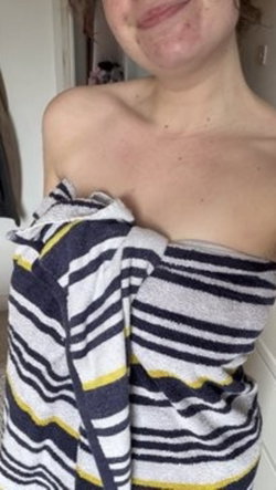 Slim woman with fair skin and freckled face wrapped in a striped towel indoors.
