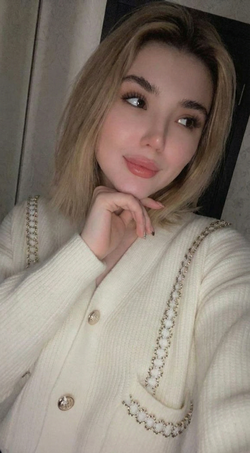 A woman with blonde hair and a white sweater poses in a mirror selfie.