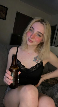 Blonde woman in black lingerie sits on a couch holding a beer bottle.