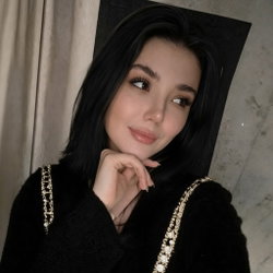 A brunette woman in a black top with a beaded design poses in a mirror selfie.
