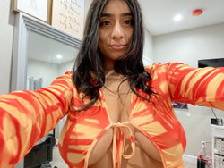 A person with long dark hair in a red and orange tiger-striped top poses in a kitchen.