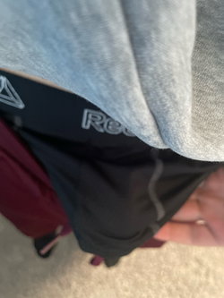 Close-up of a person wearing a gray sweatshirt and black athletic underwear with visible waistband, standing indoors on