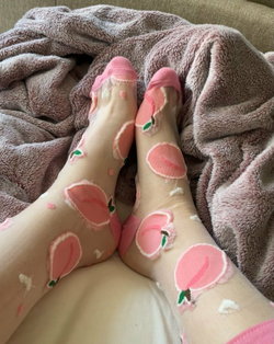 Close-up of feet wearing sheer pink peach-patterned socks, resting on a soft gray blanket.