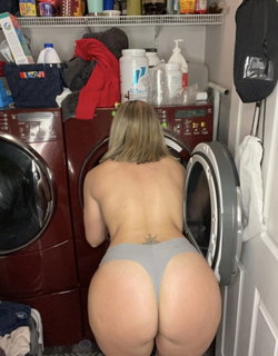 A blonde woman with a curvy body type bends over in a laundry room.
