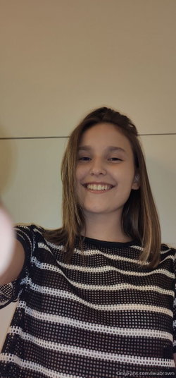 A smiling woman with shoulder-length brown hair wearing a black and white striped mesh top, taking a selfie indoors.