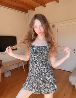Woman with long wavy brown hair wearing a floral print dress in a bright room.