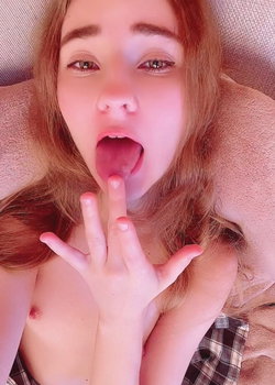 A young woman with long red hair and fair skin poses playfully in a plaid shirt.