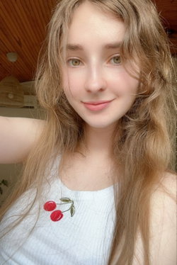 Blonde woman with long hair in a white top with cherry design.