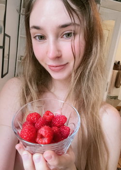 A woman with long blonde hair holds a bowl of raspberries in a cozy room.