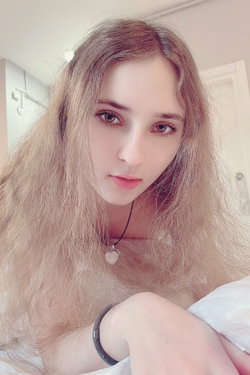 Slim woman with wavy blonde hair and necklace lies on bed in bedroom.