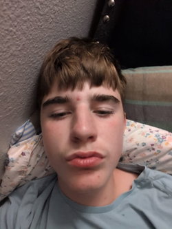 Slim man with tousled brown hair lying in bed wearing light blue t-shirt, eyes closed.