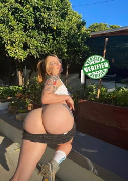 A curvy woman in black thong and white crop top poses outdoors with a verified badge.