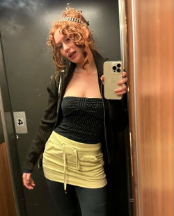 Redhead in a black top and yellow skirt taking a selfie in an elevator.