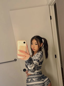 Asian woman with dark hair in a high ponytail takes a mirror selfie wearing a tight patterned sweater and matching