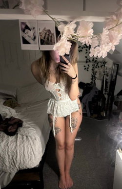 A woman in a white lace lingerie set poses in a bedroom with floral decorations.