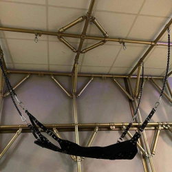 Black fabric harness suspended from metal frame with chains, no person visible.