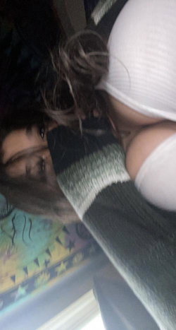 A woman with dark hair lies on her side, wearing a white top and striped sweater, partially covered by blankets in a