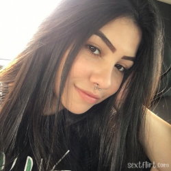 Brunette woman with long dark hair and a nose ring, wearing a black top, taking a close-up selfie indoors.