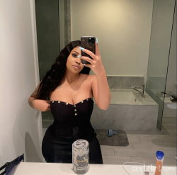 A curvy woman with long dark hair takes a mirror selfie in a black strapless top and skirt, standing in a modern