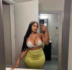 A curvy woman with long dark hair takes a mirror selfie in a sparkly white top and yellow textured skirt, standing in a