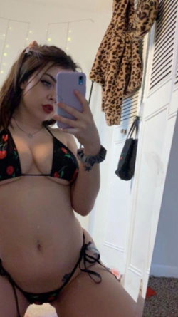 Curvy woman in floral bikini takes mirror selfie, showing midriff and hip, with leopard print robe hanging nearby.