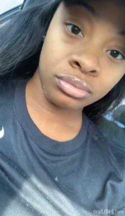 Close-up selfie of a Black woman with long dark hair, wearing a black t-shirt, inside a car.