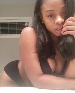 A curvy Black woman with long dark hair poses in a black bra and matching bottoms, resting her chin on her hand in a