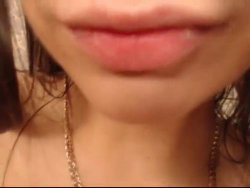 Close-up of a woman's lips and chin, wearing a delicate chain necklace with dark hair framing her face.