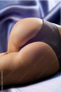 Curvy woman lying on her stomach, wearing black thong underwear, against a blue satin background.