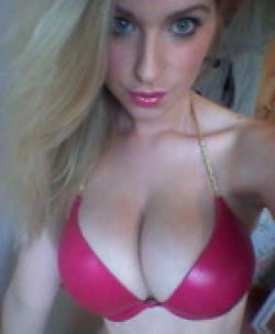 Blonde woman in a red bra takes a close-up selfie, looking directly at the camera with makeup and glossy lips.