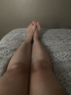 Close-up of bare legs and feet with pink toenails resting on a textured bedspread, taken from a high angle.
