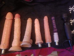 Several flesh-toned and purple sex toys arranged on a dark fabric surface with red trim.