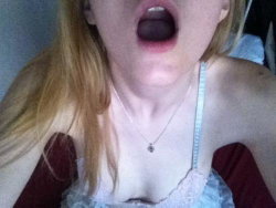 Blonde woman with open mouth, wearing a lace top and necklace, in a close-up selfie shot.