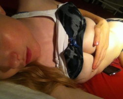 Blonde woman lying down, wearing a white top and patterned underwear, hand resting on her hip, phone nearby.