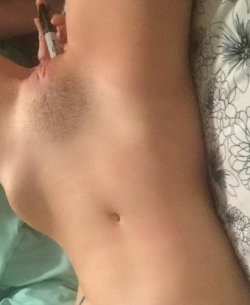 Close-up of a shirtless person's torso lying on a floral-patterned sheet, holding a small bottle near their chest.