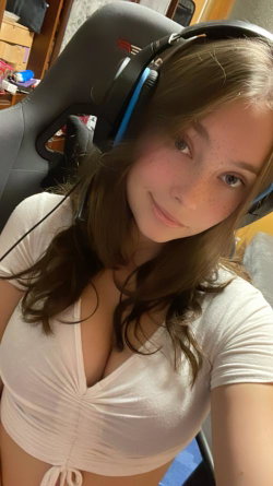 A young woman with long brown hair and freckles smiles while wearing headphones and a white crop top, seated in a