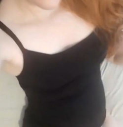 Redheaded woman in a black spaghetti strap top, partially visible from the chest up, likely indoors.