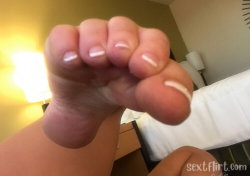 Close-up of a hand with neatly manicured nails, fingers curled into a fist, in a softly lit indoor setting with a bed
