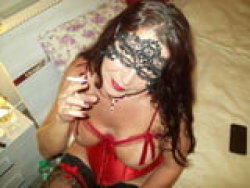 Brunette woman in red lingerie and lace mask holding a cigarette, lying on a bed with floral pillows.